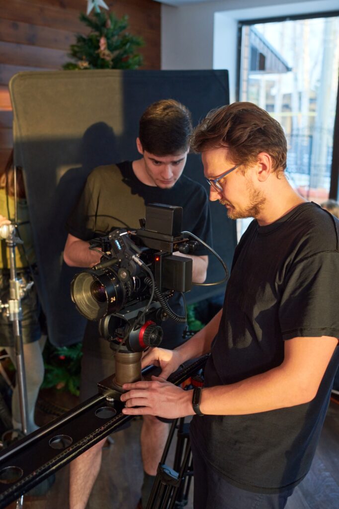 Young videographer and his assistant adjusting options of video camera