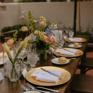Wooden table set for a wedding reception with gold chargers, white plates, and blue napkins.