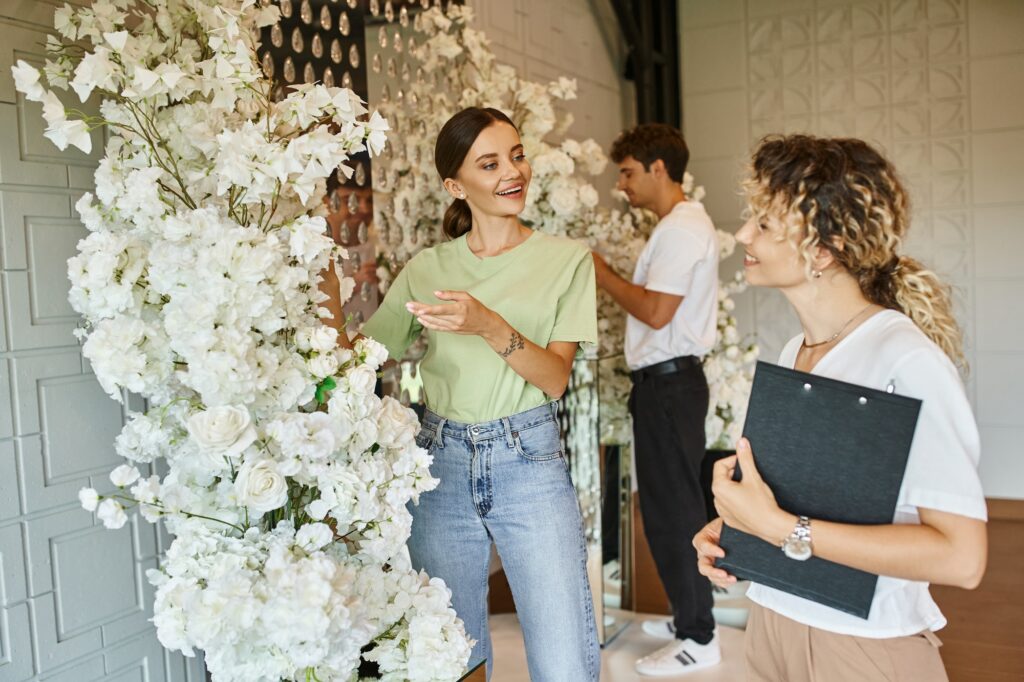 vnv events: Wedding decor ideas in Florida - "young smiling florist showing white floral decor to event manager with clipboard in event hall"