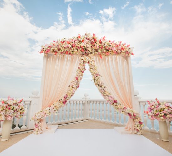 Wedding arch peach color with flowers on the background of the sea. Vases with fresh flowers.